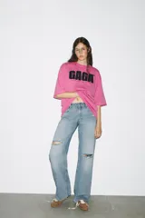 Camiseta rosa de algodón con efecto lavado, cuello redondo y manga corta. Estampado frontal con el texto "GAGA" en color negro.