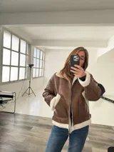 Campera marrón de cuero sintético con interior de piel sintética color crema, cierre frontal con cremallera y hebillas ajustables en el cuello y la cintura.