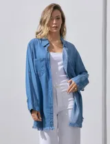 Camisa de jean celeste, marca Hester & Orchand, de corte oversize con cuello con solapa, escote en V y abertura central con botones. Delantera con bolsillos aplicados, mangas largas regulables con presilla y botón, y ruedo desflecado.