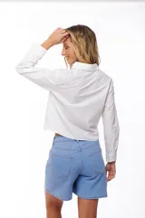 Camisa blanca de manga larga con cuello clásico y cierre frontal con botones. Presenta detalle de calado en el ruedo.