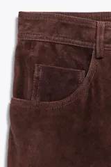 Falda midi de tiro alto confeccionada en ante color marrón chocolate, con bolsillos delanteros y traseros, abertura frontal y cierre con cremallera y botón.