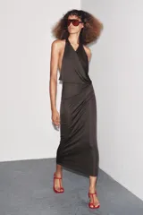 Vestido largo color marrón oscuro, de cuello halter y escote fluido. Tiene hombros descubiertos, detalle de pliegues laterales, forro interior a tono y cierre lateral con cremallera oculta y en espalda con botones.