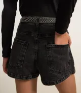 Short pollera de jeans negro con efecto marmoleado, tiro medio, trabillas y bolsillos.