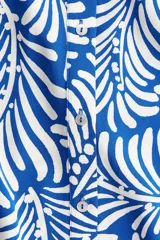 Vestido midi camisero con estampado de hojas blancas sobre fondo azul. Tiene cuello camisero, botonadura frontal, mangas cortas raglán, elástico en la cintura y cinturón extraíble para atar.