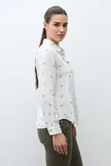 Camisa blanca de manga larga con cuello abotonado y estampado de pequeñas flores en tonos naranjas y verdes.