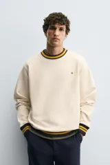 Sudadera color crema de corte regular fit, cuello redondo y manga larga. Presenta ribete a rayas en cuello, puños y bajo. Tiene un pequeño bordado de una flor en el pecho.