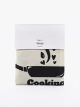 Delantal color natural con estampado de una olla y la frase "Cooking is love".