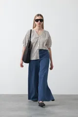 Camisa de viscosa con estampado de pequeños lunares verdes sobre fondo blanco o crema. Presenta escote en V con botones frontales y mangas cortas abullonadas con elástico en el puño.