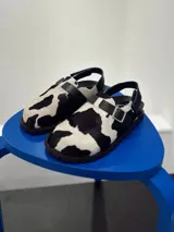 Zuecos con estampado de vaca en blanco y negro, con hebilla ajustable y suela plana.