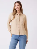 Camisa color beige de crepe, con cuello con solapa, cierre frontal con botones y dos bolsillos aplicados en el pecho.