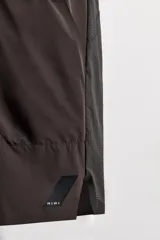 Shorts deportivos marrones de tejido técnico ligero y elástico con diferentes estructuras. Tiene forro interior, cintura elástica ajustable con cordón, bolsillos frontales, bolsillo trasero con cierre, aberturas laterales y logo estampado en la pierna.