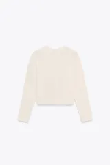 Chaqueta color crema de tejido de punto con cuello redondo y manga larga. Tiene bolsillos delanteros de plastrón y cierre frontal con botones dorados.