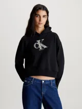 Buzo cropped negro con capucha y monograma 3D de Calvin Klein estampado en el pecho, confeccionado en algodón regenerativo.