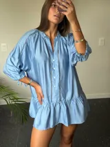 Vestido corto celeste con cuello mao, mangas 3/4 con lazo y volados en el ruedo. Tiene botones en el frente y detalles de puntilla en cuello, mangas y ruedo.