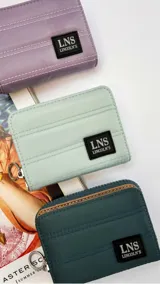 Billetera corta de tela capitoneada con cierre alrededor y tapa. Incluye varias reparticiones con tarjeteros y bolsillos, y una correa de mano desmontable. Disponible en lila, verde menta y verde oscuro.