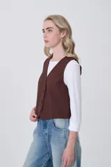 Chaleco negro de poliéster con escote en V y cierre frontal de botones. Diseño holgado.