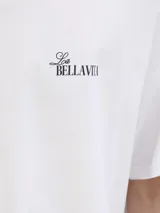 Remera blanca de algodón con cuello redondo y mangas cortas. Estampado en la espalda con una sombrilla de playa, una reposera y la frase "Bella Vita".
