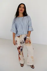 Pantalón de lino color celeste con estampado de flores grandes en tonos marrones, azules y rojos. El pantalón es de corte ancho y tiene cintura alta con cordón ajustable.