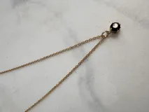 Collar dorado con dije de piedra facetada negra.