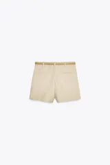 Bermuda color crema de tiro medio con pinzas delanteras y cinturón fino color beige. Tiene bolsillos frontales y falsos bolsillos de vivo en la espalda.