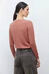 Sweater color rosado melange con cuello redondo y manga larga. Presenta un bordado abstracto en color crema en la parte frontal.