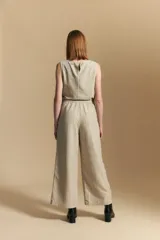 Pantalón de vestir de tiro alto, color beige claro con finas rayas verticales oscuras. Es de corte ancho y largo, con un lazo de tela a juego anudado en la cintura. Se combina con un top sin mangas del mismo tejido y color.
