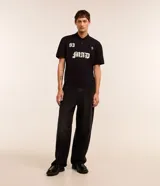 Remera boxy de mangas cortas, confeccionada en algodón, color negro, con cuello polo y lettering "93 MAD" y una cruz estampada en la parte delantera.
