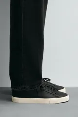 Zapatilla urbana de cuero sintético color negro, con cordones y suela de goma color crema.