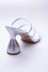 Sandalias plateadas con taco de forma geométrica y tiras transparentes.