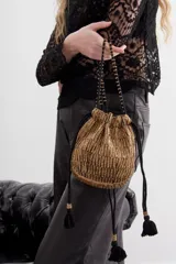 Cartera de noche tipo bolso redondo, confeccionada con lentejuelas y canutillos dorados brillantes. Cuenta con borlas de ajuste, cordón de ajuste con terminaciones en hilo y una correa al tono con apliques de canutillos.