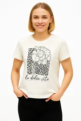 Remera color crema de manga corta y cuello redondo, con estampado de flores y leopardo, y la frase "lo dolce vita".