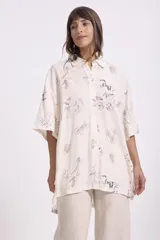 Camisa beige con estampado abstracto en tonos grises, azules y marrones. Corte oversize, mangas cortas y cuello clásico.