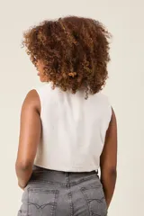 Chaleco cropped color crema, confeccionado en lino, con cuello camisero, cierre frontal con botones, dos bolsillos con solapa en el pecho y lazo ajustable en la cintura.