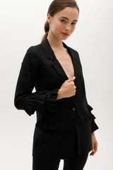 Blazer negro de lino con solapas, cierre frontal con un botón, bolsillos delanteros con solapa y mangas largas con volantes en los puños.