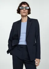 Blazer azul marino de corte entallado, con cuello de solapa de muesca, manga larga, hombros estructurados, dos bolsillos de ribete en la parte delantera, detalle de pinzas, abertura posterior y forro interior.