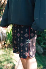 Short de baño negro con estampado geométrico en tonos naranja y blanco, con ribete rojo en el ruedo y logo de la marca en la pierna izquierda.