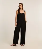 Mono de mujer color rojo oscuro (bordó), de corte recto y pierna ancha, con escote corazón y tirantes anchos con elástico. Presenta pliegues frontales que caen rectos hasta el ruedo.