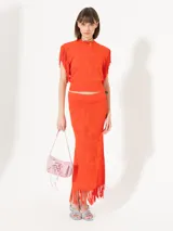 Top color naranja tejido con calados, sin mangas y con flecos en las sisas.