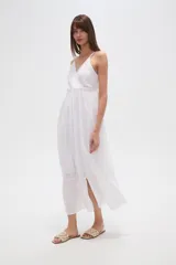 Vestido largo blanco de algodón con broderie, escote en V cruzado y breteles finos. Presenta un corte entallado en la cintura con elástico y falda fluida con tajo lateral.