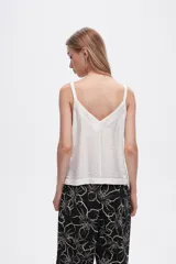 Musculosa blanca de bretel ancho con cuello en V y detalle de ojales metálicos en los tirantes. Corte al cuerpo.