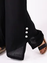 Pantalón palazzo negro con cintura elástica y cordón ajustable. Presenta aberturas laterales con botones blancos.