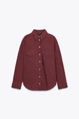 Camisa color borgoña a rayas verticales finas, de corte recto, con cuello solapa y manga larga. Tiene dos bolsillos de parche con solapa en el pecho y cierre frontal con botones.