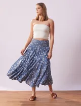 Falda midi de algodón estampada con flores blancas sobre fondo azul. Tiene pretina ancha elastizada en punto smock, ruedo con volados y forro interno a tono.