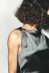 Vestido midi de satén color gris oscuro, con escote asimétrico, manga sisa, detalle de aplique dorado en el hombro y frunces laterales.