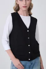 Chaleco de punto color crema, con cuello en V, cierre frontal de botones y dos bolsillos frontales.