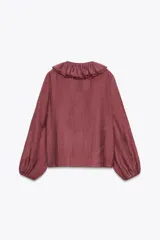 Blusa color crudo confeccionada en hilatura con mezcla de lyocell. Escote pico ajustable con cordones, manga larga con volumen acabada en elástico y detalle de volantes en el mismo tejido.