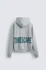 Sudadera gris con capucha ajustable, corte boxy fit, manga larga, bolsillo tipo canguro y estampado en la espalda.