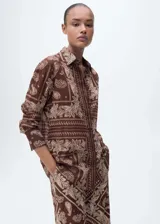 Camisa marrón con estampado paisley en tonos beige, de corte recto, cuello camisero y mangas largas con puños abotonados.