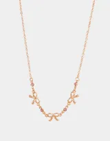 Collar corto bañado en oro rosa con cadena de eslabones y tres dijes de moño con strass rosado.