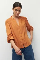 Camisa color naranja con cuello mao, escote en V, botones forrados y mangas largas con puños elásticos.